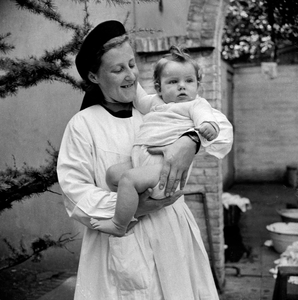 823252 Portret van een Zuster Augustinesse met een baby op de arm, op de achterplaats van het Klooster Genazzano ...